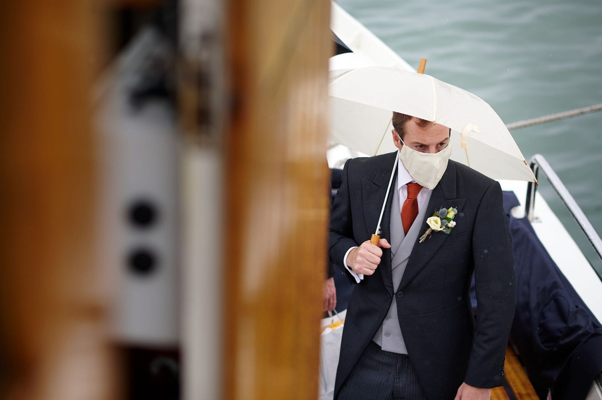 Groom wearing a mask carrying an umbrella on brownsea Island