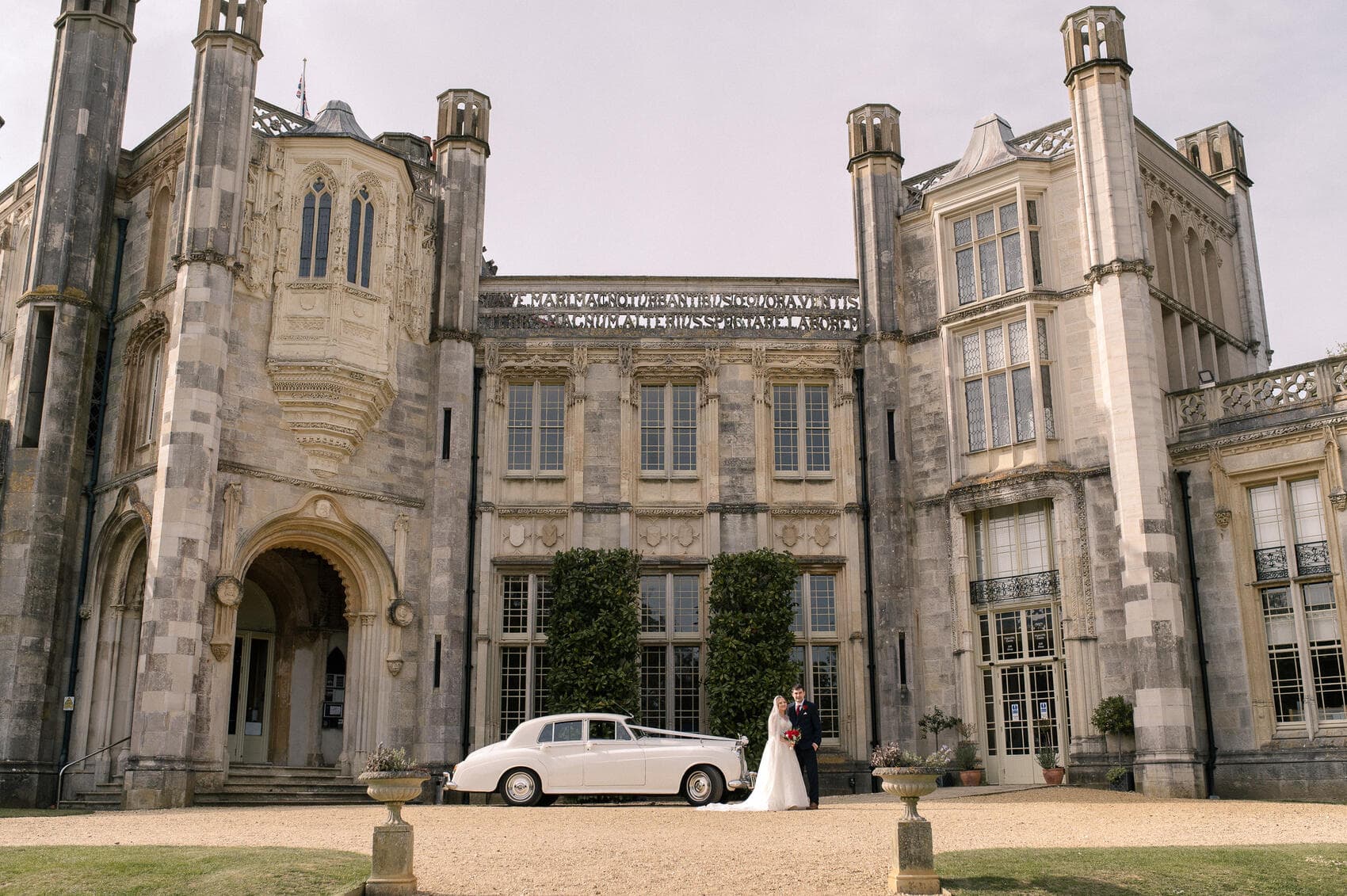 Bride and groom outside with their car at Highcliffe castle wedding