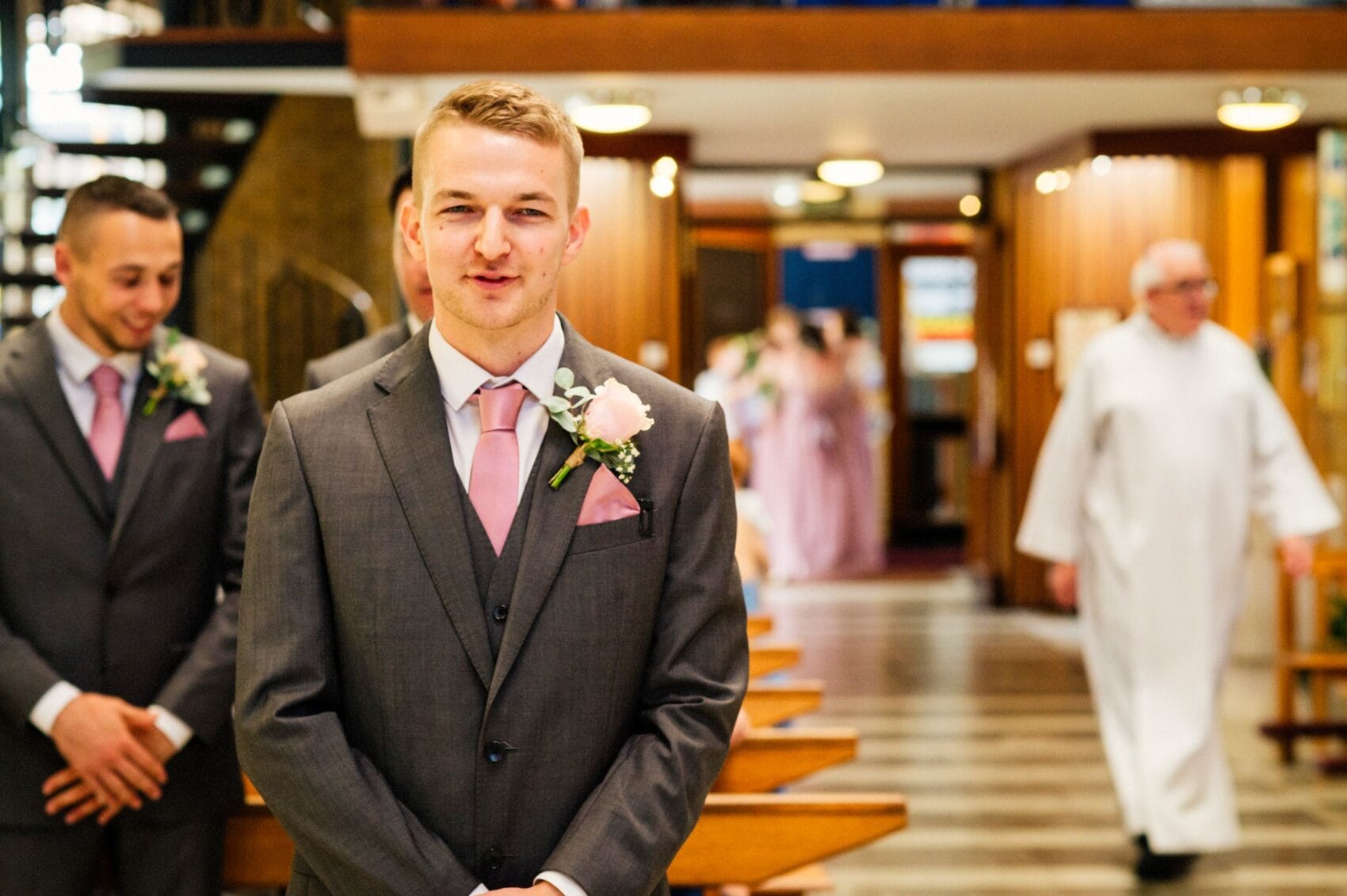 Groom, Ben, smiles at the bridemaids wait in the background of St Mary's Catholic Church