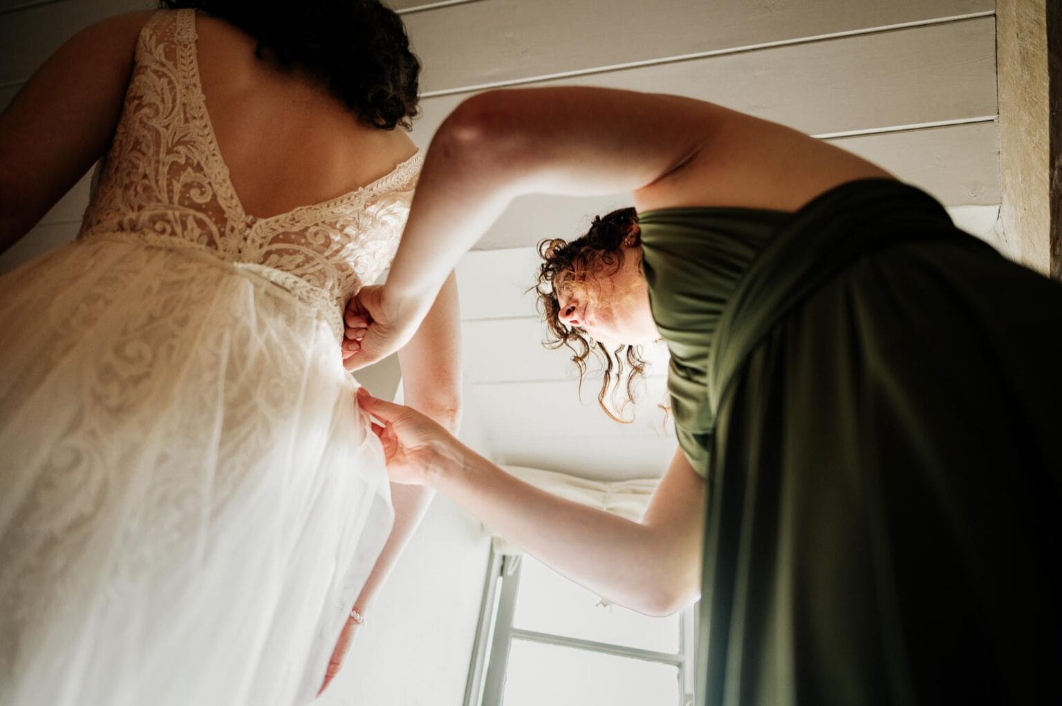 Bridesmaid finishes the buttoning up of the dress at River Cottage wedding