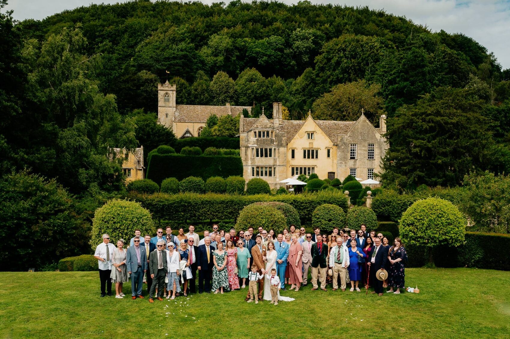 Wedding party pose in front of the manor from the tiered gardens at Owlpen Manor.