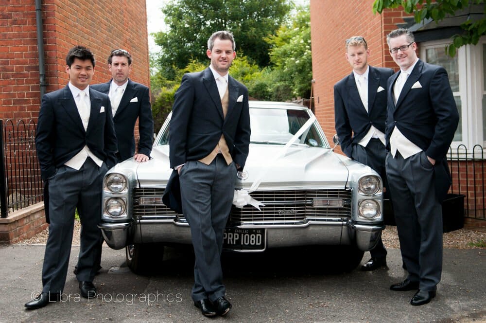 Groom and ushers pose by american car