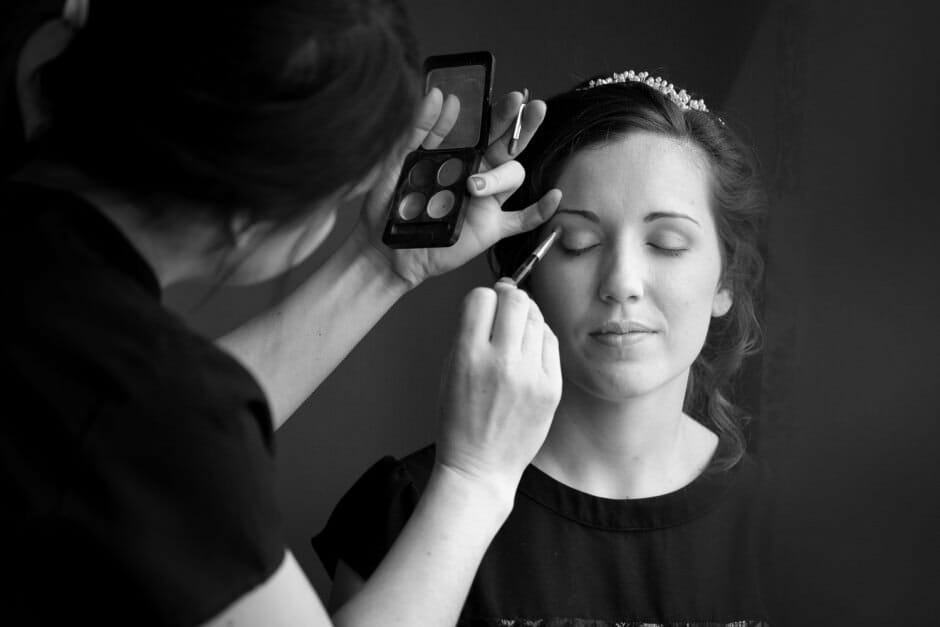Bride having makeup applied by window