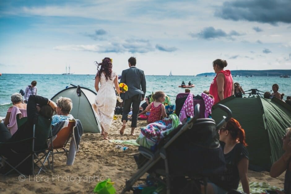 Bride and groom walk through crowded Bournemouth beach